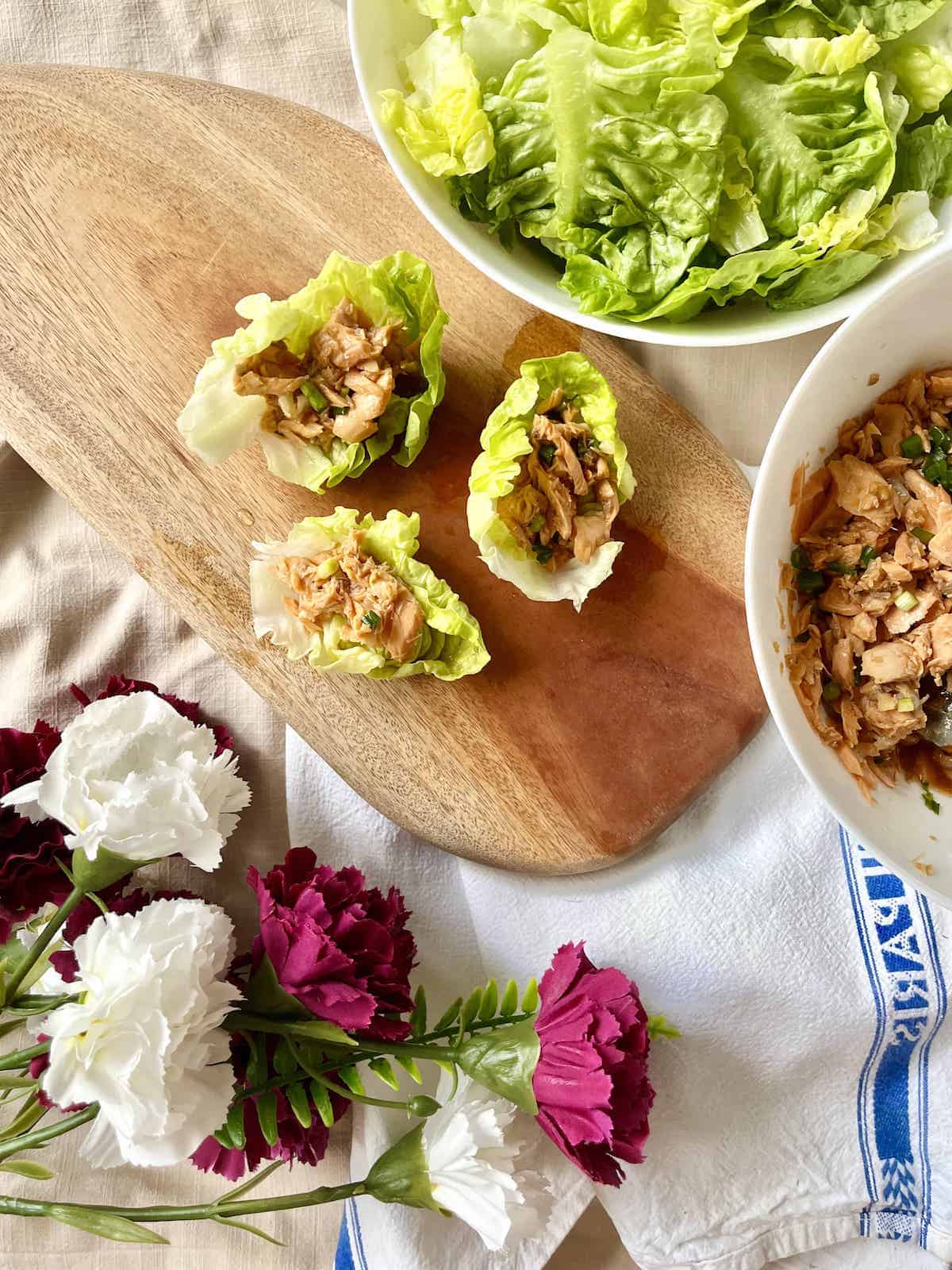 3 salmon lettuce wraps next to a bowl of salmon and lettuce.